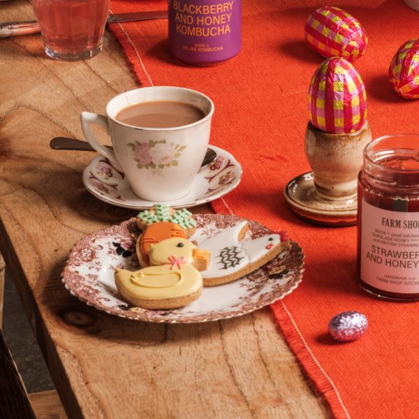 Colourful iced bisuits on a china plate with a cup of tea behind, on a decorated Easter table