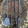 trio of stainless steel barbecue tools on a tree stump